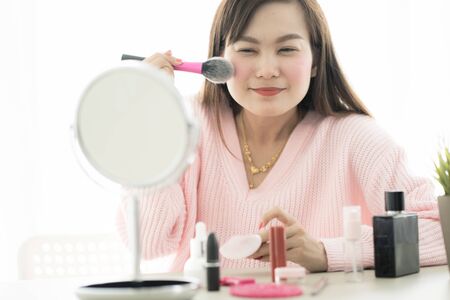 Asian woman looking to mirror doing makeup at homeの写真素材