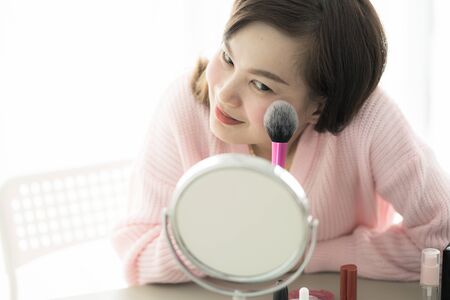 Asian woman looking to mirror doing makeup at homeの写真素材