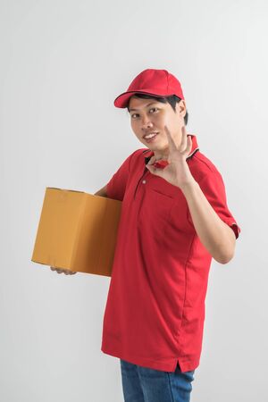 Young smiling logistic delivery man in red uniform holding the box on white backgroundの写真素材