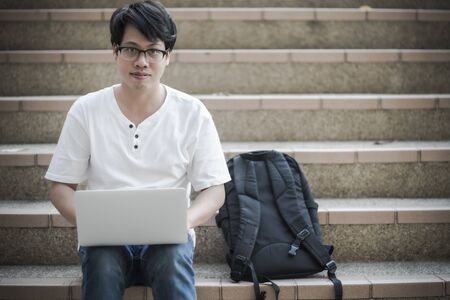 Young man sitting on the stairs using laptop. Asian peopleの写真素材