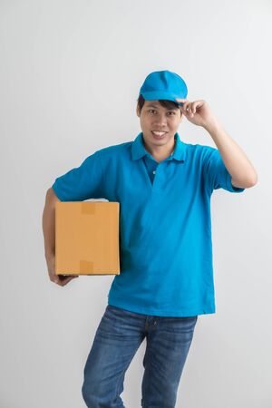 Young smiling logistic delivery man in blue uniform holding the box on white background. Asian peopleの写真素材