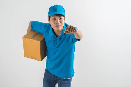 Young smiling logistic delivery man in blue uniform holding the box on white background. Asian peopleの写真素材