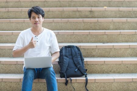 Young man sitting on the stairs using laptop. Asian peopleの写真素材