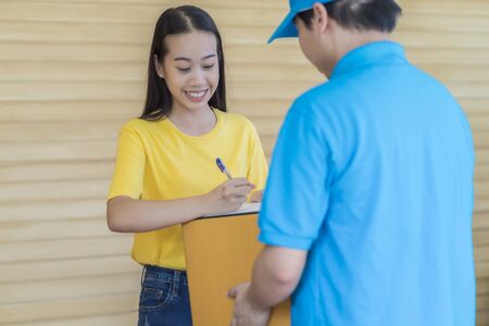 Asian woman receiving a package at home from a delivery guyの写真素材