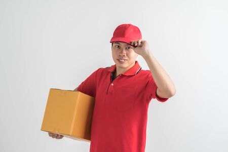 Young smiling logistic delivery man in red uniform holding the box on white backgroundの写真素材