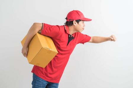Young smiling logistic delivery man in red uniform holding the box on white backgroundの写真素材
