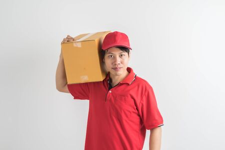 Young smiling logistic delivery man in red uniform holding the box on white backgroundの写真素材