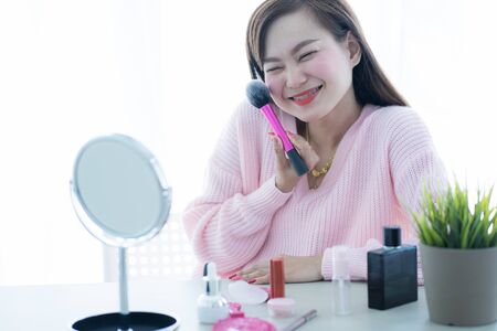 Asian woman looking to mirror doing makeup at homeの写真素材