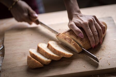 Fresh bread on the kitchen table The healthy eating and traditional bakery concept. Whole grain bread put on kitchen wood plate with a chef holding gold knife for cut. Fresh bread on table close-upの写真素材