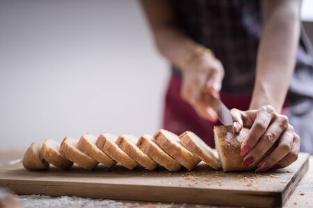 Fresh bread on the kitchen table The healthy eating and traditional bakery concept. Whole grain bread put on kitchen wood plate with a chef holding gold knife for cut. Fresh bread on table close-upの写真素材