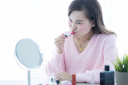 Asian woman looking to mirror doing makeup at homeの写真素材
