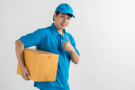 Young smiling logistic delivery man in blue uniform holding the box on whiteの写真素材