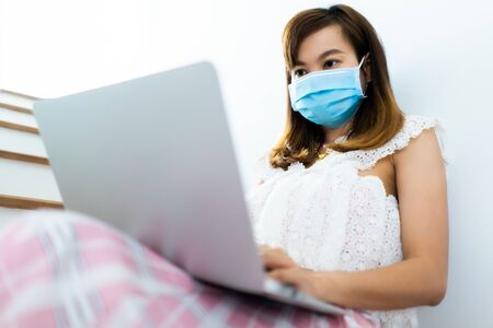 Asian woman working or learn from home with laptop and medicine health care mask on stairの写真素材