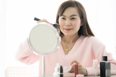 Asian woman looking to mirror doing makeup at homeの写真素材