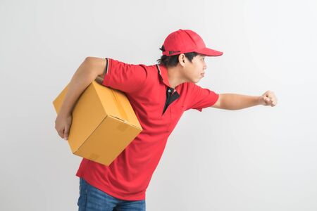 Young smiling logistic delivery man in red uniform holding the box on white backgroundの写真素材