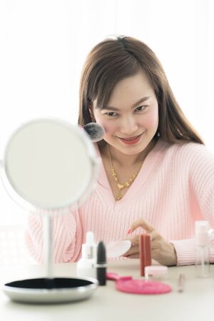 Asian woman looking to mirror doing makeup at homeの写真素材