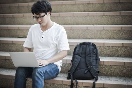 Young man sitting on the stairs using laptop. Asian peopleの写真素材
