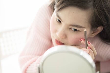 Asian woman looking to mirror doing makeup at homeの写真素材