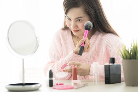 Asian woman looking to mirror doing makeup at homeの写真素材