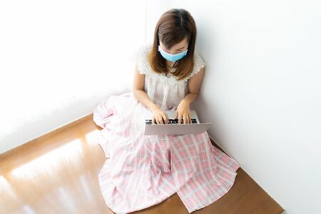 Asian woman working or learn from home with laptop and medicine health care mask on stairの写真素材