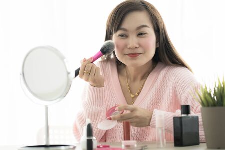 Asian woman looking to mirror doing makeup at homeの写真素材