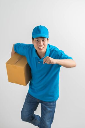 Young smiling logistic delivery man in blue uniform holding the box on white background. Asian peopleの写真素材