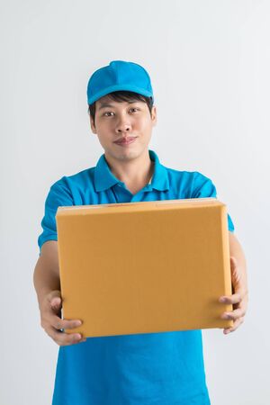 Young smiling logistic delivery man in blue uniform holding the box on white background. Asian peopleの写真素材
