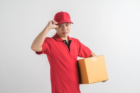 Young smiling logistic delivery man in red uniform holding the box on white backgroundの写真素材
