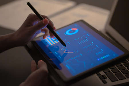 Asian business woman reviewing data in financial charts and graphs with tablet. Accounting