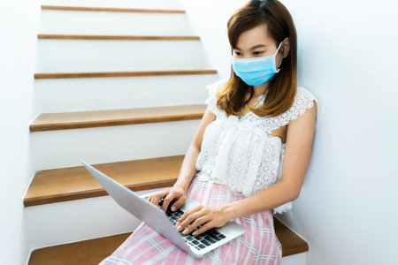 Asian woman working or learn from home with laptop and medicine health care mask on stairの写真素材