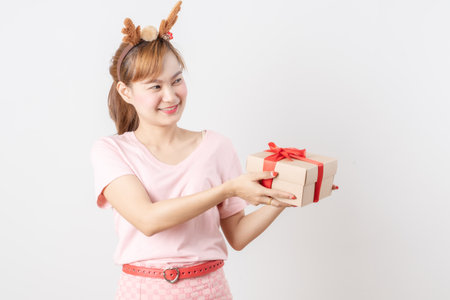 Asian woman is wearing christmas reindeer antlers holding big giftbox in hands grey background.の写真素材