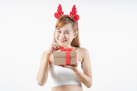 Asian woman is wearing christmas reindeer antlers holding big giftbox in hands grey background.の写真素材