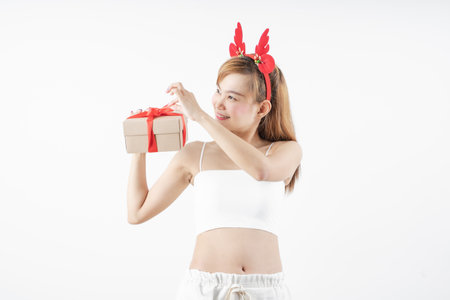 Asian woman is wearing christmas reindeer antlers holding big giftbox in hands grey background.の写真素材