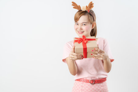 Asian woman is wearing christmas reindeer antlers holding big giftbox in hands grey background.の写真素材