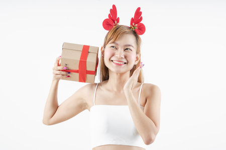 Asian woman is wearing christmas reindeer antlers holding big giftbox in hands grey background.の写真素材