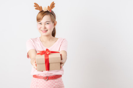 Asian woman is wearing christmas reindeer antlers holding big giftbox in hands grey background.の写真素材