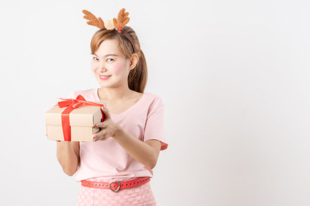 Asian woman is wearing christmas reindeer antlers holding big giftbox in hands grey background.の写真素材