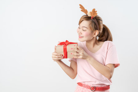Asian woman is wearing christmas reindeer antlers holding big giftbox in hands grey background.の写真素材