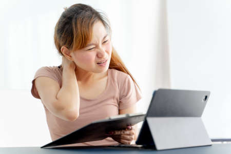 Young asian businesswoman feeling pain in neck after working on computer laptop for a long time. Office syndrome conceptの写真素材