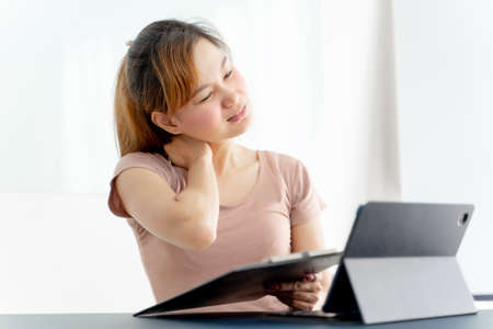 Young asian businesswoman feeling pain in neck after working on computer laptop for a long time. Office syndrome conceptの写真素材