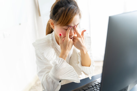 Asian businesswoman massaging eyes feeling strain fatigue headache relieving pain, eyesight problem, exhausted female worker suffering from migraine eyestrain after computer work, overwork conceptの写真素材