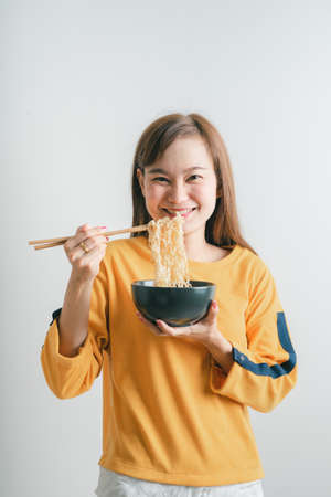 Asian girl holding a bowl of noodles with chopsticks and eating it, isolated on white backgroundの写真素材