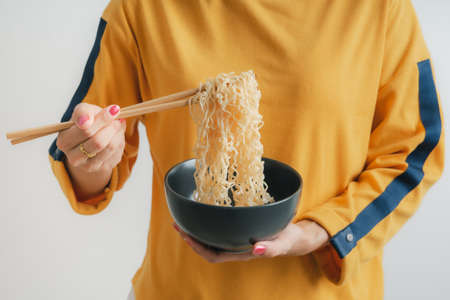 Asian girl holding a bowl of noodles with chopsticks and eating it, isolated on white backgroundの写真素材