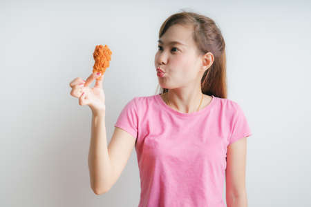 Young asian woman holding and eating fries chicken on white backgroundの写真素材
