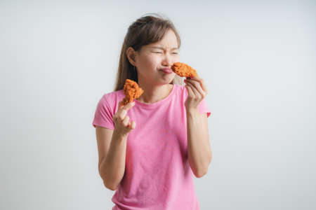 Young asian woman holding and eating fries chicken on white backgroundの写真素材