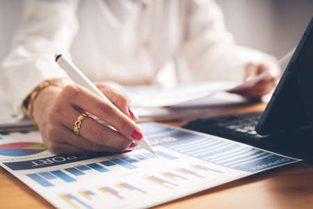 Business woman reviewing data in financial charts and graphs on wooden desk in office and business working, tax, accounting, statistics and analytic research conceptの写真素材