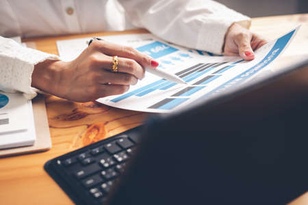 Business woman reviewing data in financial charts and graphs on wooden desk in office and business working, tax, accounting, statistics and analytic research conceptの写真素材
