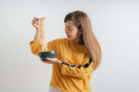 Asian girl holding a bowl of noodles with chopsticks and eating it, isolated on white backgroundの写真素材