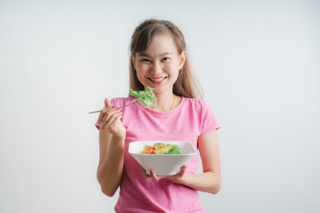 Asian woman eating a fresh salad isolated on whiteの写真素材