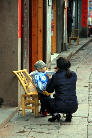 Fenghuang, China, March 23, 2012 - A Chinese woman feeding an infant in a street of Fenghuangのeditorial素材